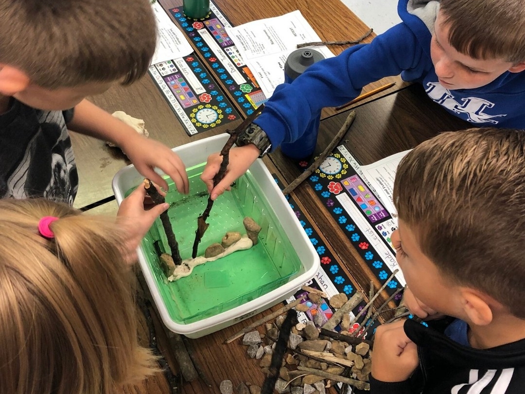 Elementary school kids making a beaver dam out of common household items.