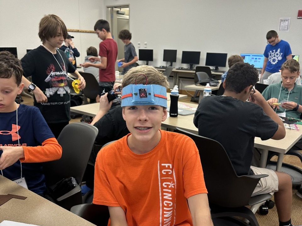 Makers in the Middle Camp A middle school child wears a handmade microbit-powered headband with fellow campers in the background.