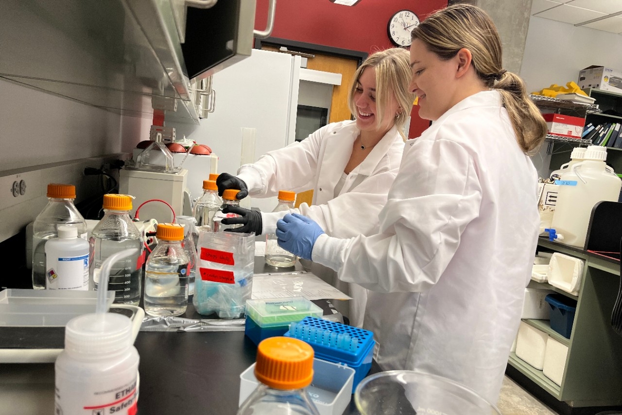 STEM students in lab coats conduct research in a biology lab.