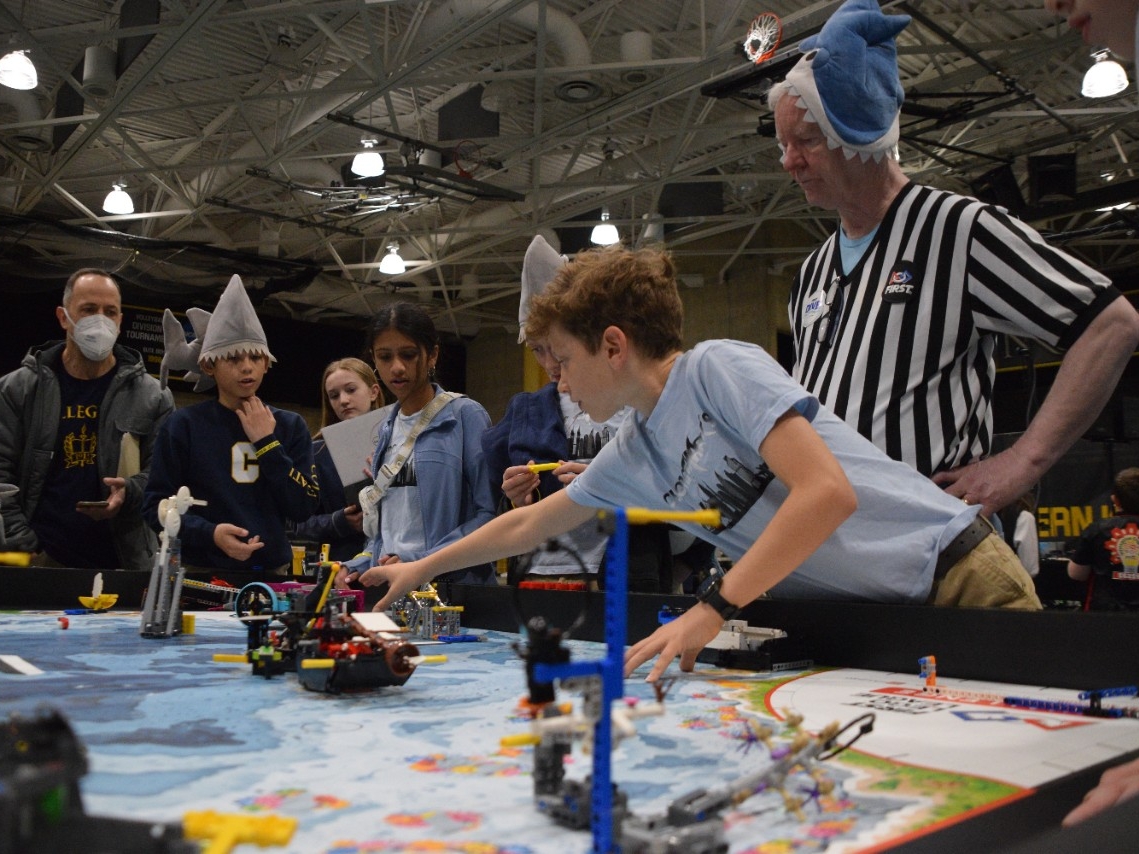 Elementary aged students wearing fun shark hats intently watch their team's LEGO robot perform at the annual Kentucky robotics competition at Northern Kentucky University.
