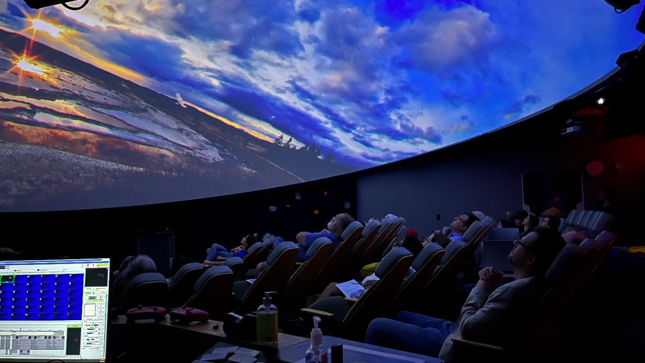Planetarium visitors gaze at the dome-shaped screeen which featuring a vibrant sunset.