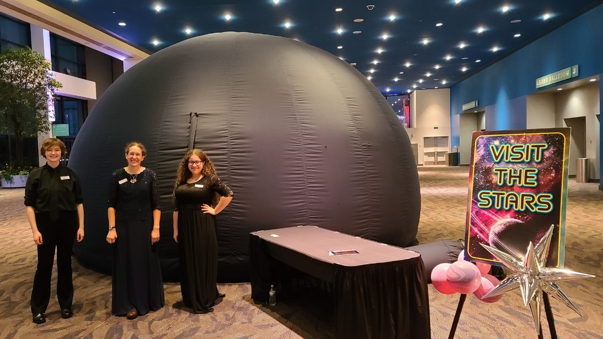 Planetarium staff smile in front of the Roaming Dome at a private event in a convention center.
