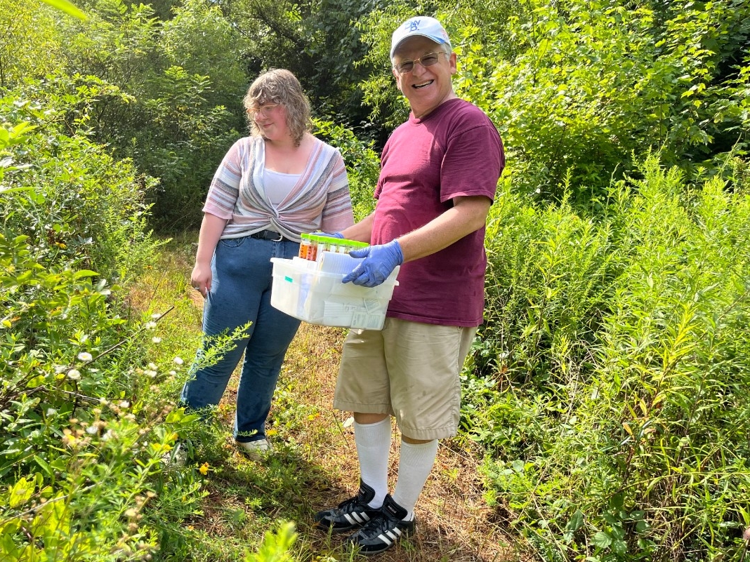Dr. Mester collects samples in a field with a student researcher.