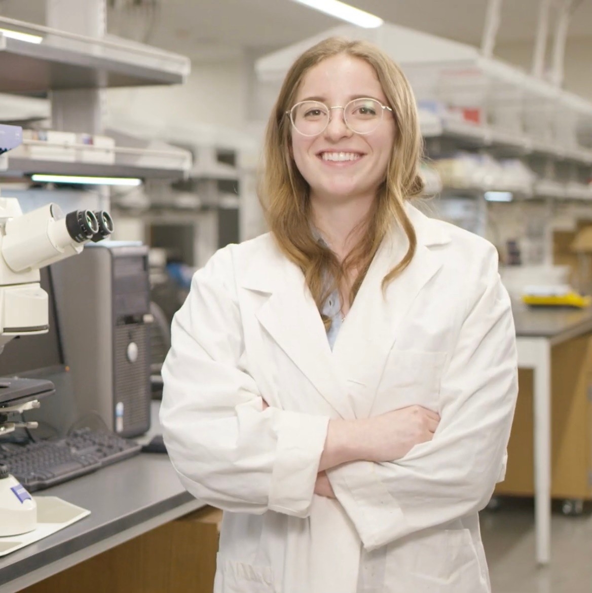Katie Sawvell smiles in the laboratory wearing her lab coat.