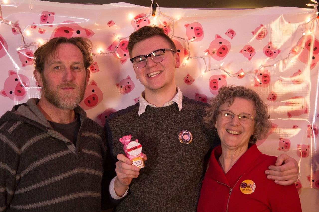 Image of an OINK film festival winner smiling with a man and woman while holding a trophy.