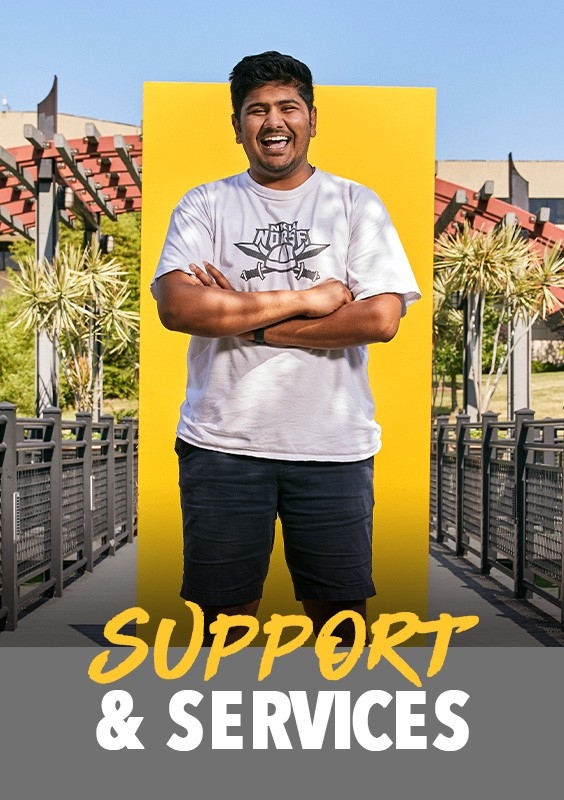 Student support: Student standing in front of a yellow panel with campus buildings behind in the background