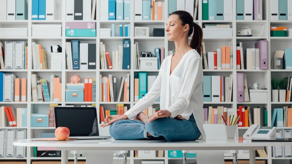Woman practicing meditation on a desk Woman sitting on a desk meditating